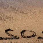 Main écrivant une carte postale sur serviette de plage ensoleillée
