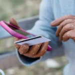 Main tenant une carte bancaire bloquée devant un smartphone affichant un numéro d'urgence