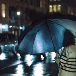 Rue parisienne sous la pluie avec parapluies et vitrines illuminées d'un café