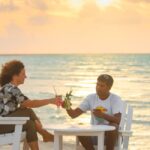 Couple sur une plage ensoleillée avec valises, départ last minute tout inclus