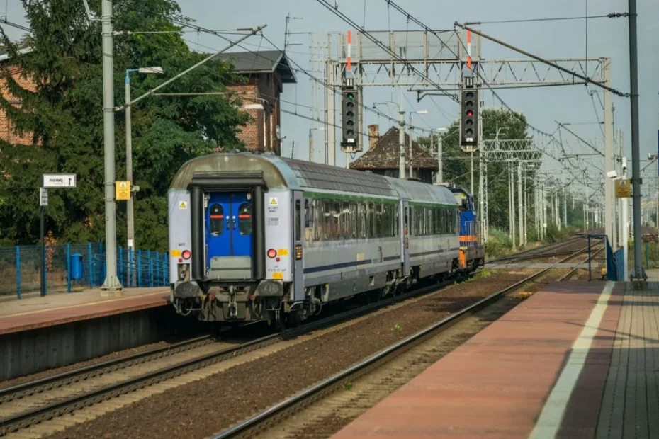 Une femme en fauteuil roulant devant une gare avec valise, assistée