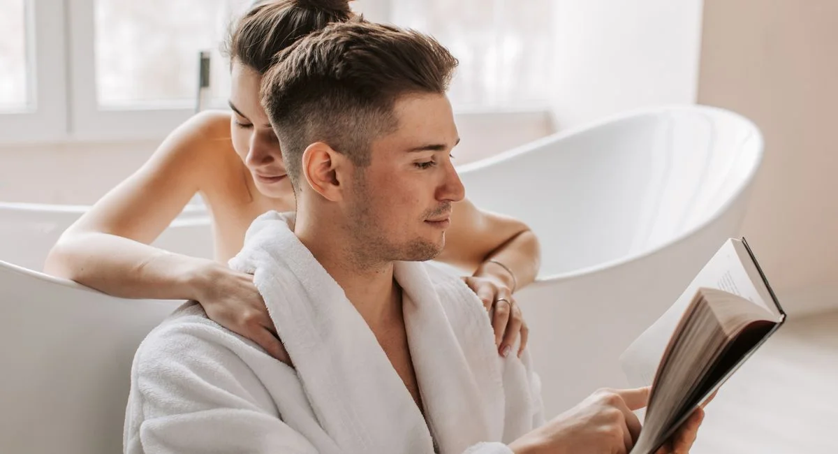 A couple enjoying a relaxing moment in a bathroom with a book and warm embrace.