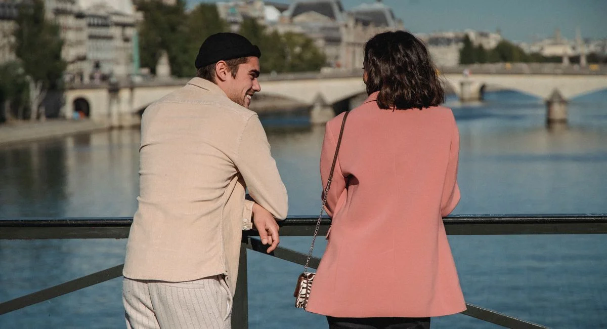 A couple enjoying a scenic view from a bridge overlooking a river on a sunny day.