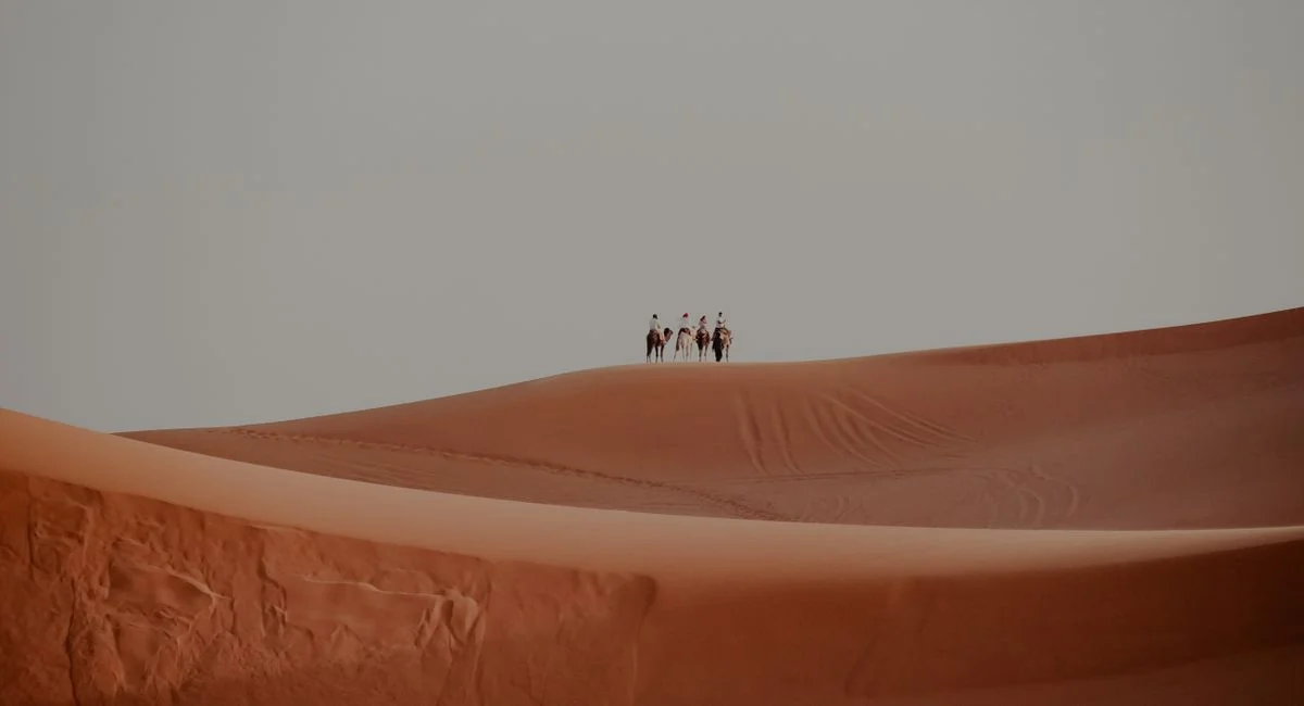 A group of people riding camels across vast dunes in Marrakesh, Morocco, showcasing a serene desert landscape.