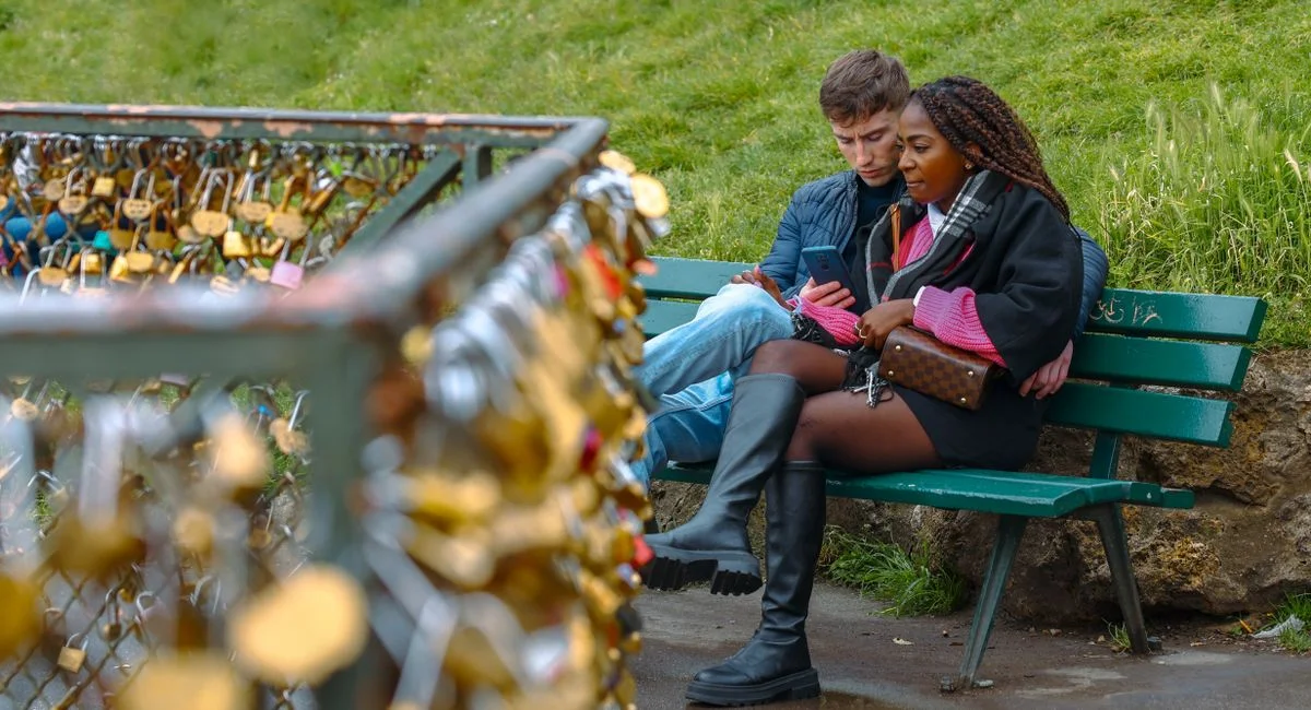 Couple seated by love locks in Paris, surrounded by lush greenery.