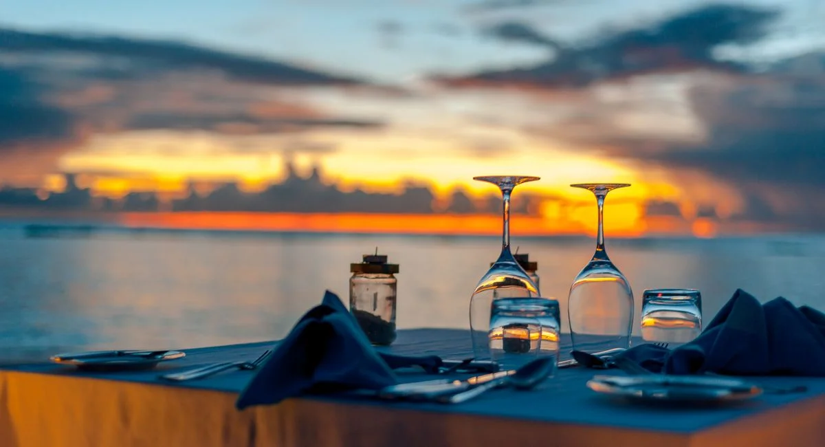 Elegant dinner setup by the ocean during a stunning sunset, creating a romantic ambiance.