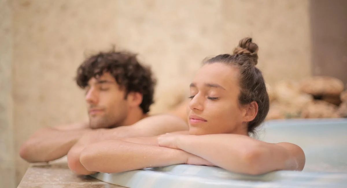 Happy cheerful man and woman with closed eyes bathing together leaning on bath edge during romantic weekend in luxury hotel i