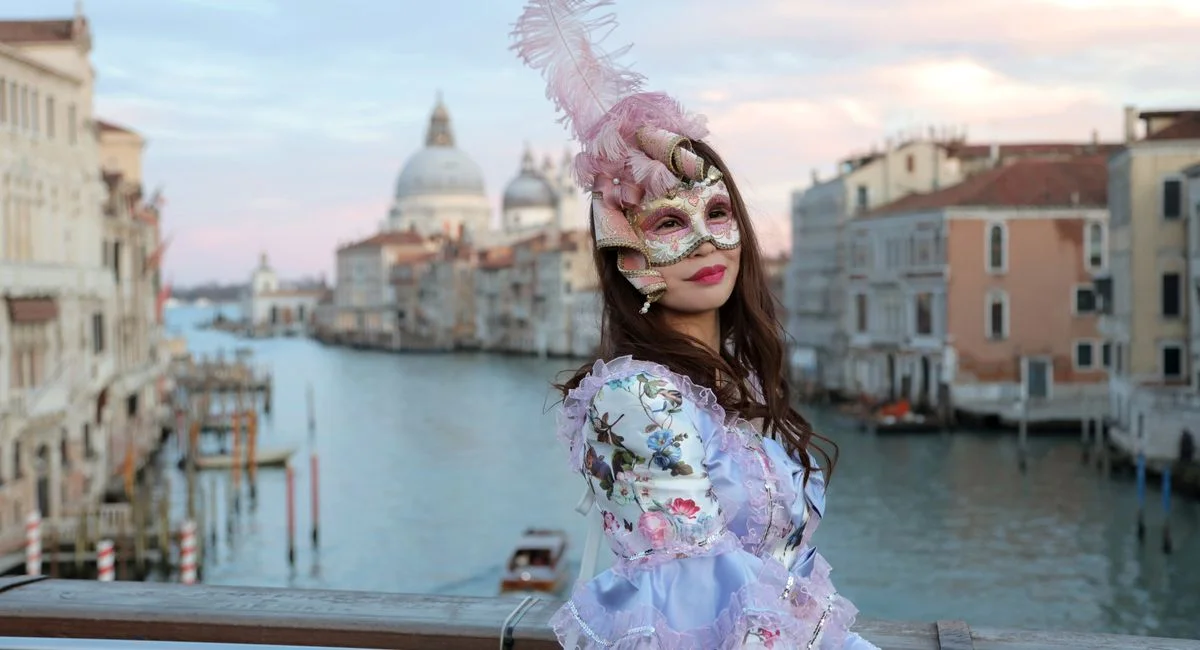 Side view of unrecognizable woman in magnificent costume and gorgeous Venetian mask with feathers standing on bridge in middl