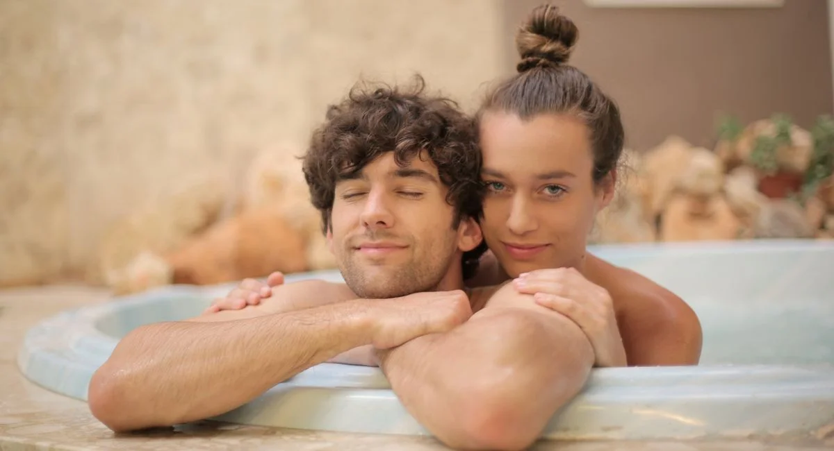 Young cheerful man and woman taking bath together enjoying holidays on blurred background of spa resort with marble interior 