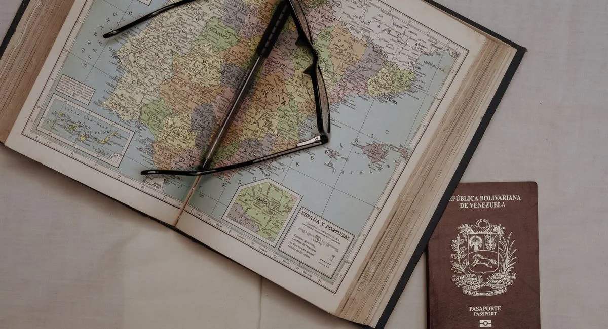 A vintage map of Spain with eyeglasses and a Venezuelan passport, symbolizing travel planning.